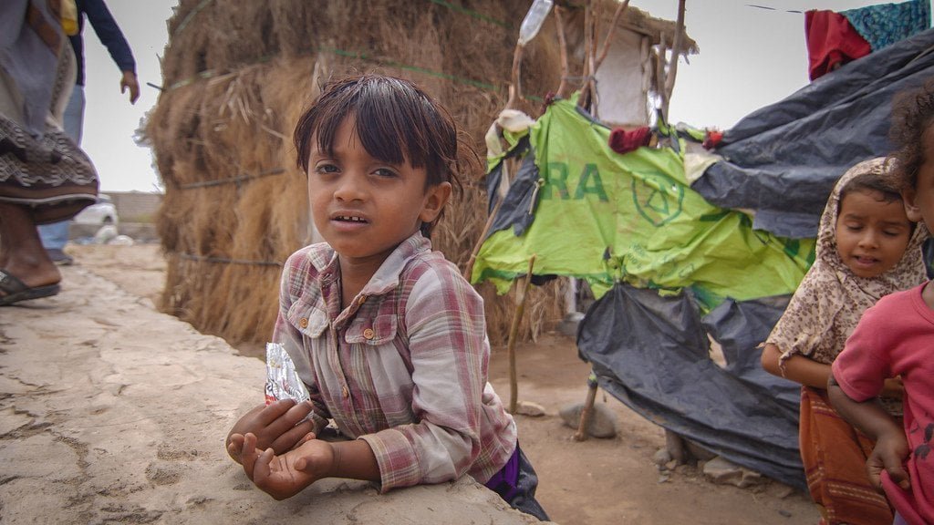 A young boy plays while his mother lines up at a water point in a camp for displaced people in Aden, southern Yemen.