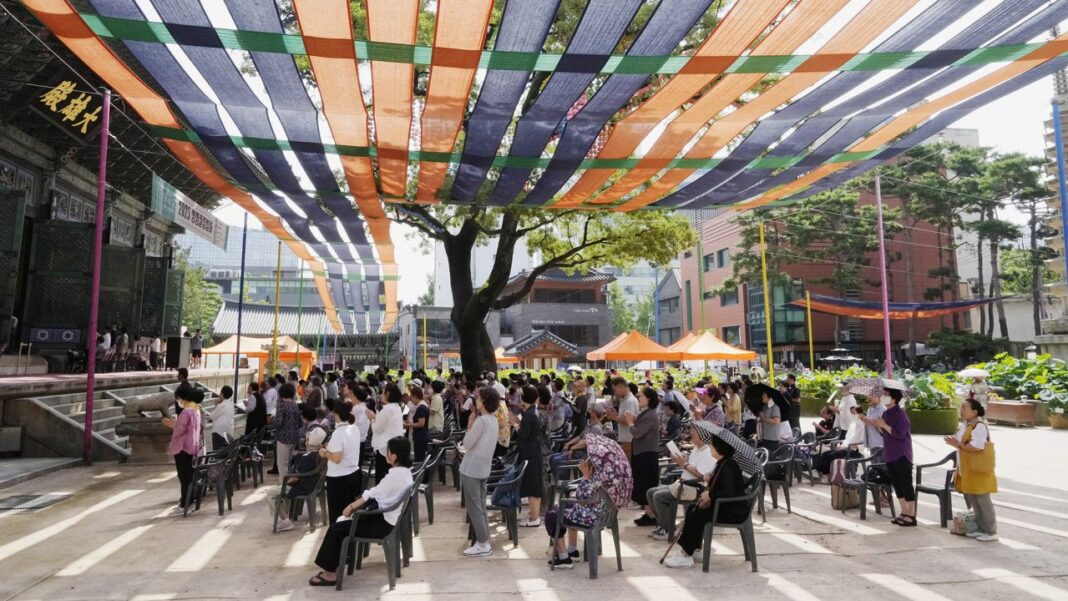 People pray under a sunshade to avoid the heat at the Chogye temple in Seoul on Wednesday.