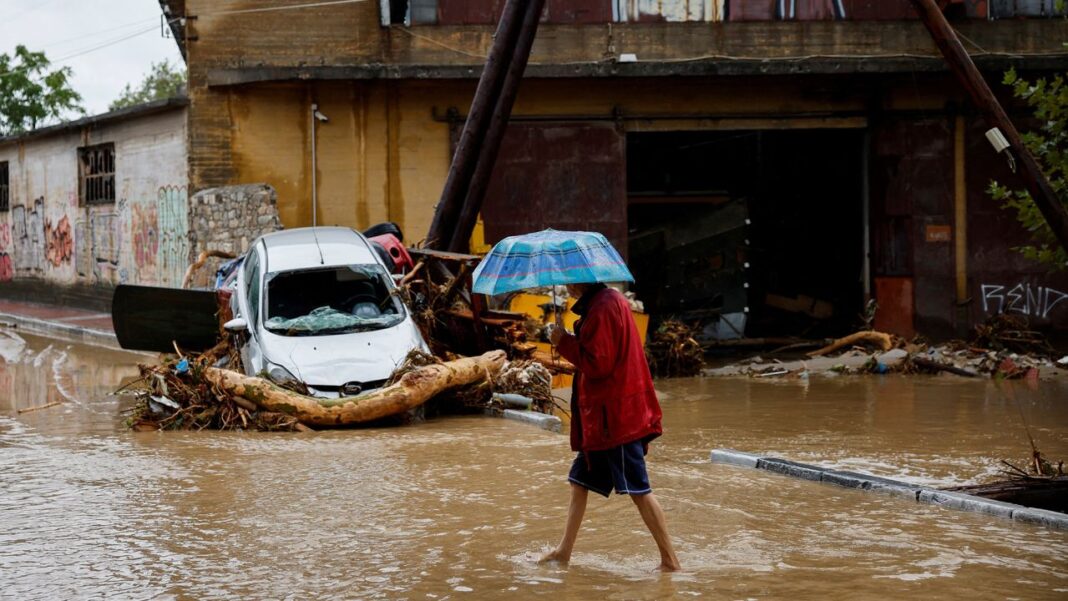 A man holding an umbrella walks on a flooded road in Volos, Greece.