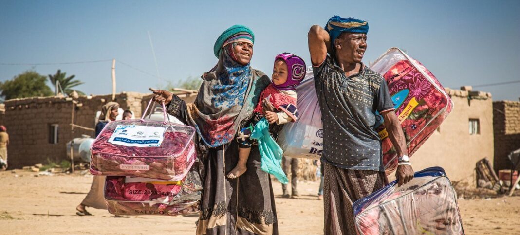 A displaced family in Marib, Yemen, carries a winter aid package back to their shelter.